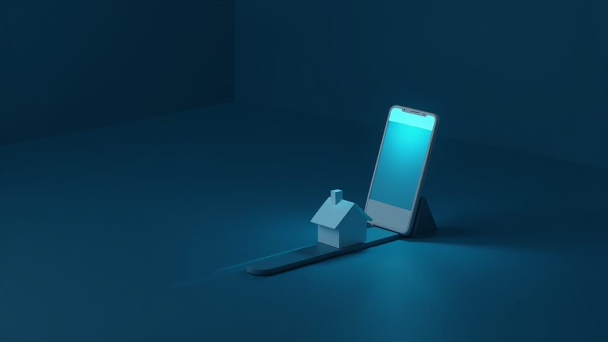 A phone standing behind a small house model on a short lit path