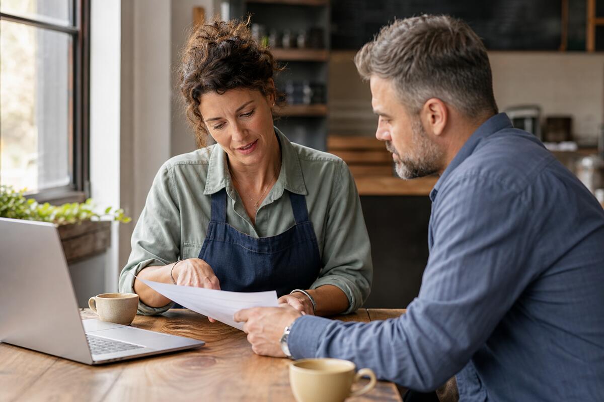 A small business owner and consultant reviewing a printed quote beside a laptop at a wooden desk